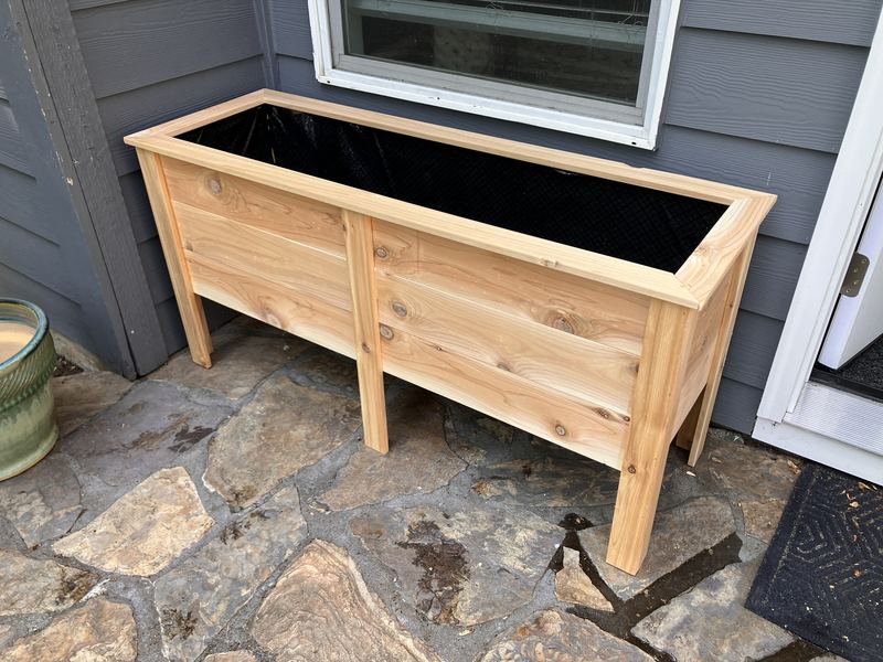 The same tall custom planter box, empty with a black liner, before planting