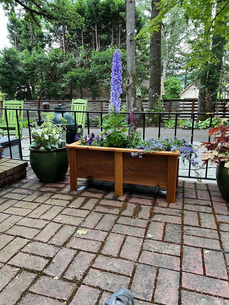 A long cedar planter box on a brick patio surrounded by potted plants