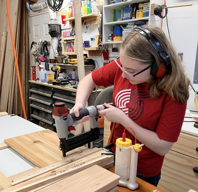 Greg's daughter in safety glasses and ear protection using a nail gun on cedar boards